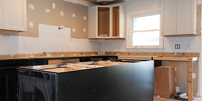 A bare kitchen with black bottom cabinets, patched walls and white wall cabinets. 