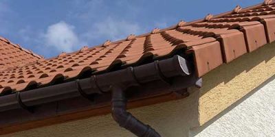 Brown Gutters and Downspout Attached to House with Clay Roof Tiles.