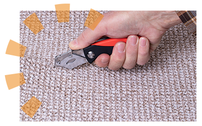 Bare hand cuts middle of old carpet with utility knife.