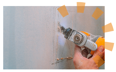 Hands using saw to cut bathroom drywall.