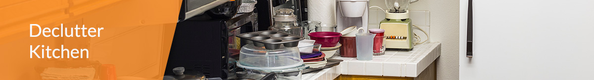 A kitchen with white tile counters that are heavily cluttered with pots, pans, cleaning materials, glasses, plates and other items.