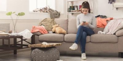 Woman Looking at Her Phone While Sitting on a Cluttered Couch