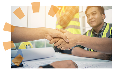 A person shakes hands with a contractor with a set of blueprints sitting on a table.