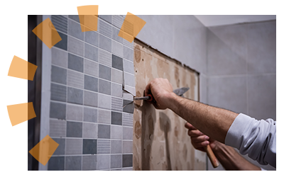 Homeowner hands using chisel and hammer to remove bathroom vanity tile during remodel.