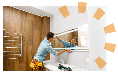 Dark-haired man homeowner with utility belt carefully removing mirror from bathroom wall.