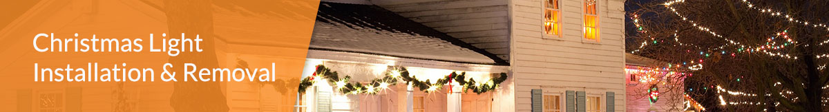 Image of a colonial house with a fence out front strung up with Christmas lights.