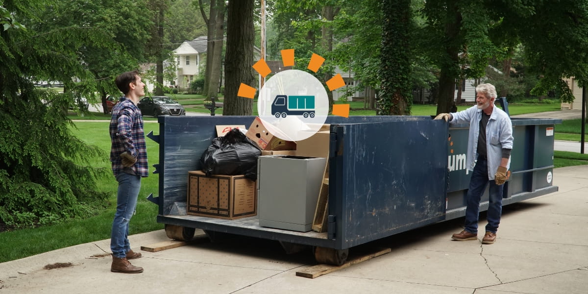 Two men standing near a loaded roll off dumpster in a driveway.