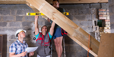 Three men measuring space between basement studs for insulation. 