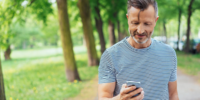 A man looks at his phone while walking down a sidewalk.