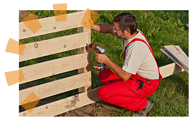A man installs a wooden fence in a yard.