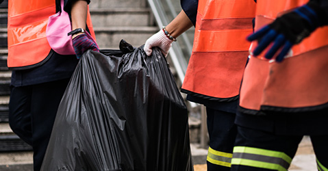 Three junk removal workers carrying bags of trash