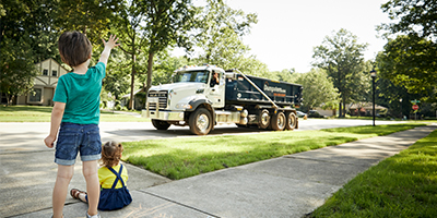 Kids waving at a Dumpsters.com dumpster truck