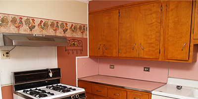 Old wooden kitchen cabinets with a salmon colored countertop and backsplash.