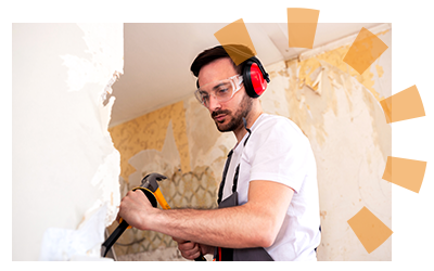 Man knocking down drywall with tools and ear covers.
