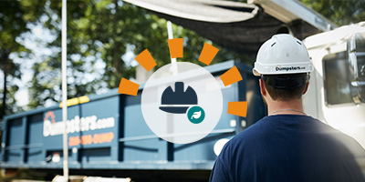 Worker in a white hard hat standing in front of a white service truck hauling a Dumpsters.com roll off bin.