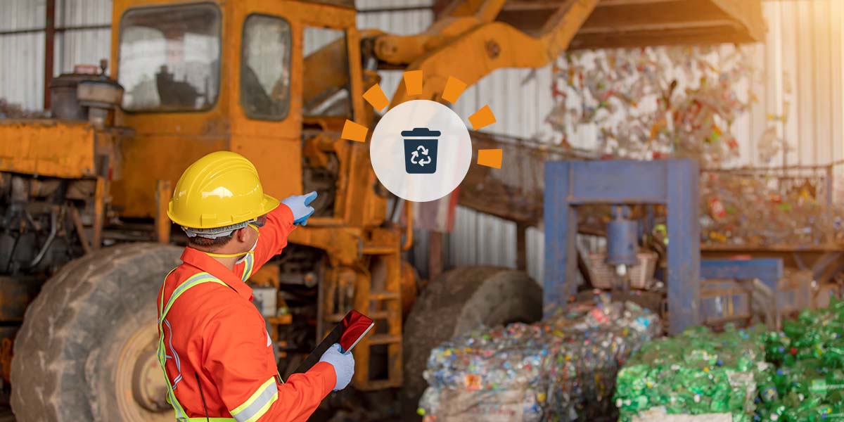 A man in a yellow hardhat directing a tractor at a recycling plant.