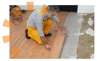 Man crouched down installing flooring in basement.