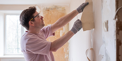 A man removing wallpaper in his home. 