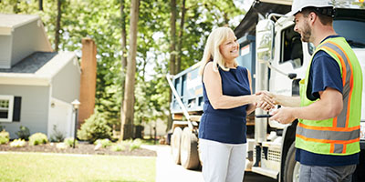 A Dumpsters.com driver shaking hands with a woman in a blue shirt after picking up a roll off dumpster. 