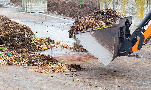 Heavy machinery is used to move a pile of green waste at a composting landfill facility.