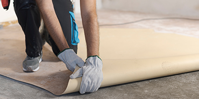 A person rolling out a sheet of linoleum for installation.