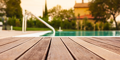 Old wooden deck in foreground with blurred pool and house in the background.