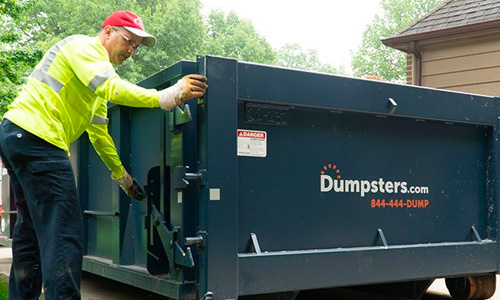 A delivery driver demonstrates how to open the swinging door of a blue Dumpsters.com roll off dumpster.