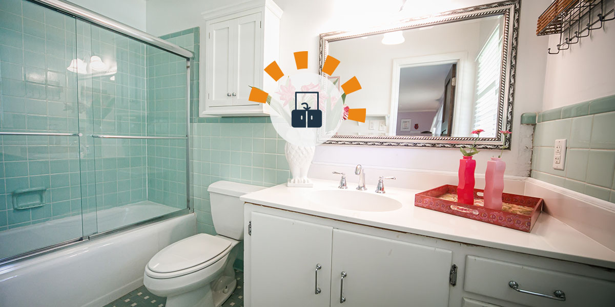 Outdated bathroom vanity and sink with mint green tiles and old countertop and white cabinets.