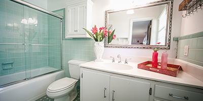 Outdated bathroom vanity and sink with mint green tiles and old countertop and white cabinets.