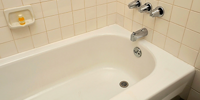 Outdated off-white plain bathtub and surrounding tile.