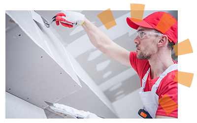 Man in red uniform patching where ceiling meets the wall.