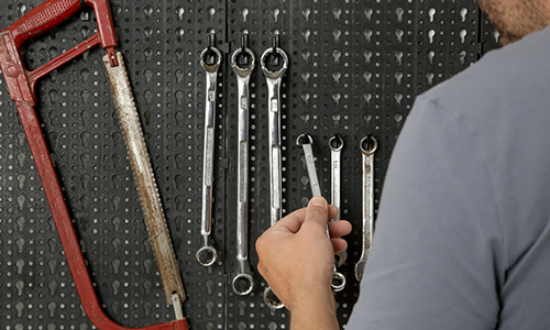 A man hangs tools on a black pegboard next to a saw.