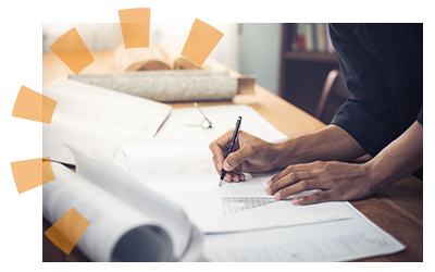 Person using a pen while standing over a desk covered in blueprints.