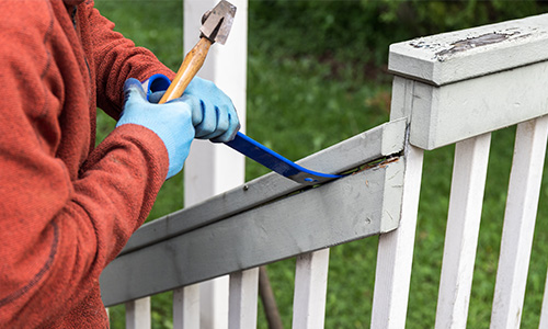 The rail of a porch is removed with a hammer and pry bar.