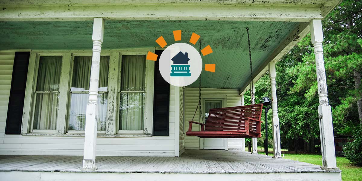 An old white wooden porch attached to a two-story home.