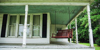 An old white wooden porch attached to a two-story home.