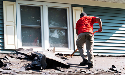 A man pulls shingles off the roof of a porch.