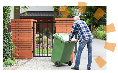 A man in a plaid shirt and jeans pushing a green garbage can to the curb