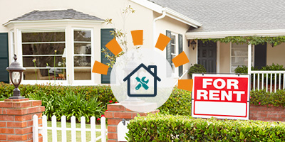 Red for rent sign on white wooden stake in front lawn of yellow multi-story house with front porch.