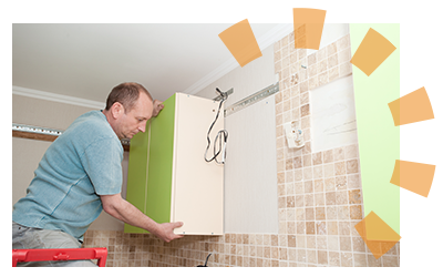 A man in a blue shirt pulls lime green cabinets away from a kitchen wall.