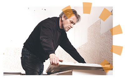 A man in a black shirt removes a white countertop from lower kitchen cabinets.