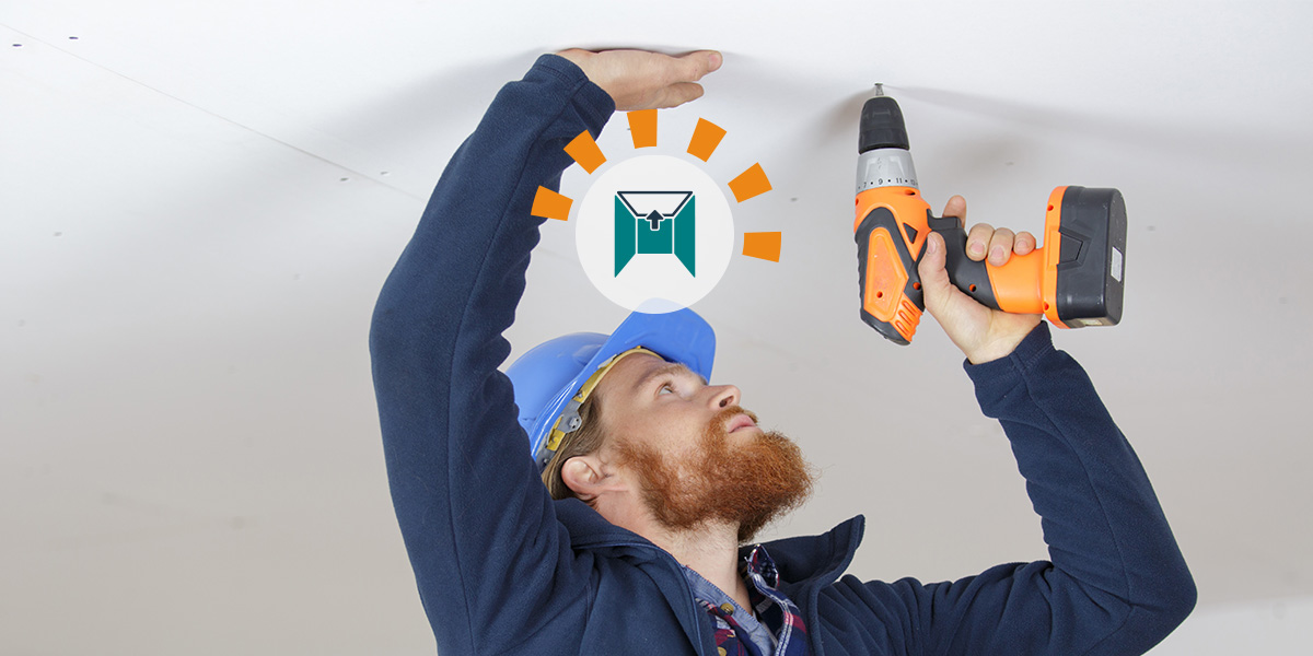 A man screws a drywall panel to the ceiling.