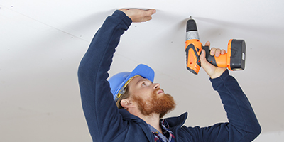 A man screws a drywall panel to the ceiling.