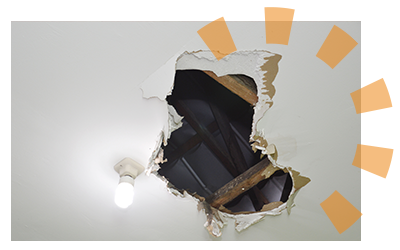 A hole in ceiling drywall exposing joists.