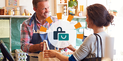 A male cashier in an apron handing a reusable bag to a woman.  