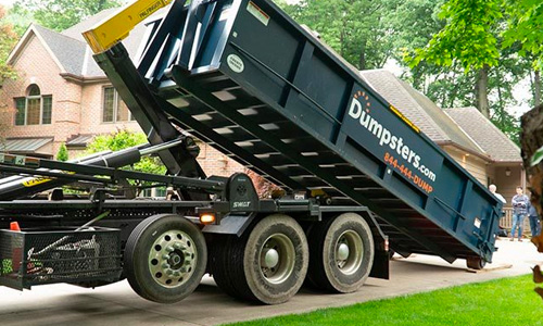 A blue Dumpsters.com roll off dumpster is placed in a driveway.