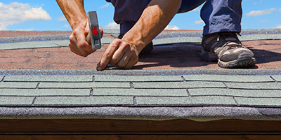 A man hammers asphalt shingles on a roof.