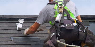 A roofer working on an asphalt shingled roof while attached to a safety harness.