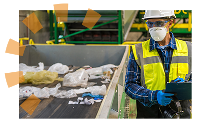 Worker wearing a hard hat and mask analyzing trash in a processing facility.