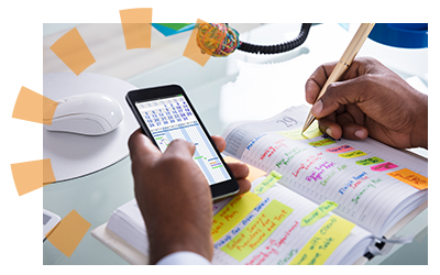 A man using his phone and notebook to mark a date in his calendar. 